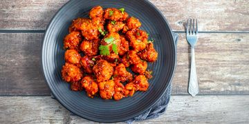 Spicy fried cauliflower bites garnished with herbs on a black plate.