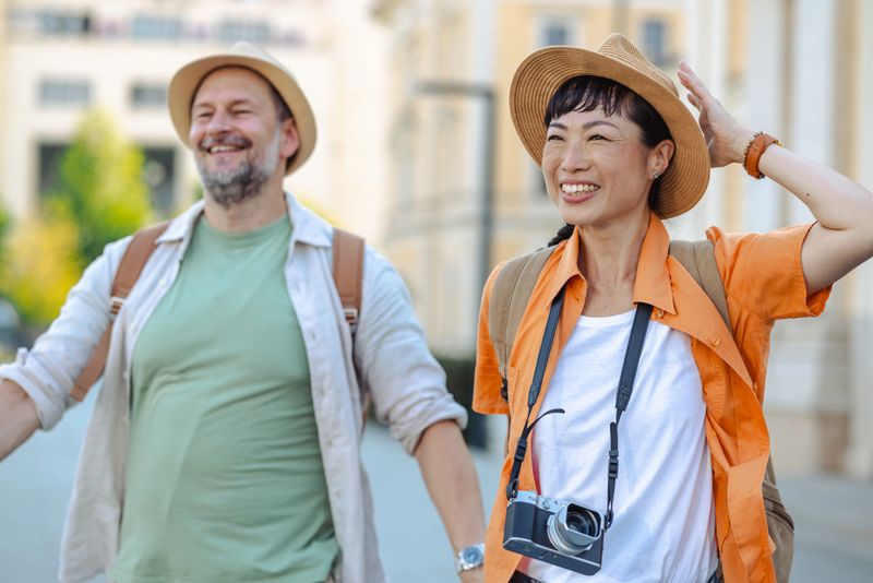 Two individuals wearing casual travel attire engage in friendly interaction outdoors on a sunny day.