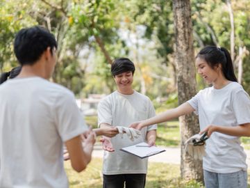 Young volunteers exchanging gloves and clipboard in park.