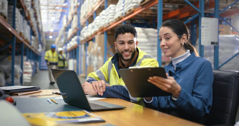 Business people, distribution and laptop with conversation, clipboard and logistics. Employees, coworking and warehouse for export, documents and tech with internet, supply chain and check schedule