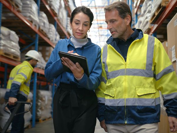 Two warehouse workers reviewing inventory on a tablet.