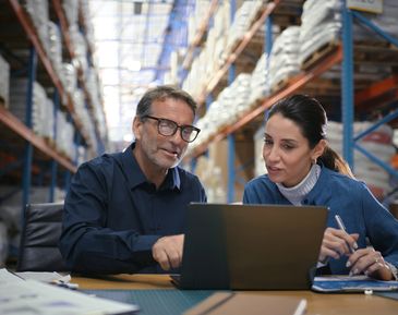 Two colleagues discussing work on a laptop in a warehouse.