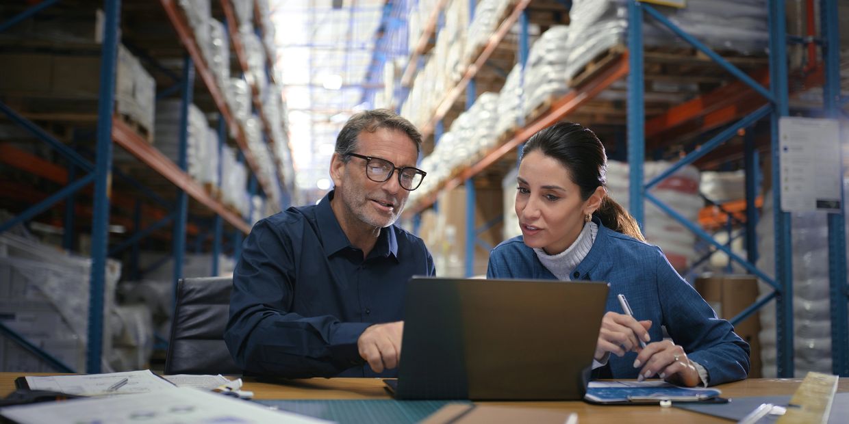 Two colleagues discuss work on a laptop in a warehouse.