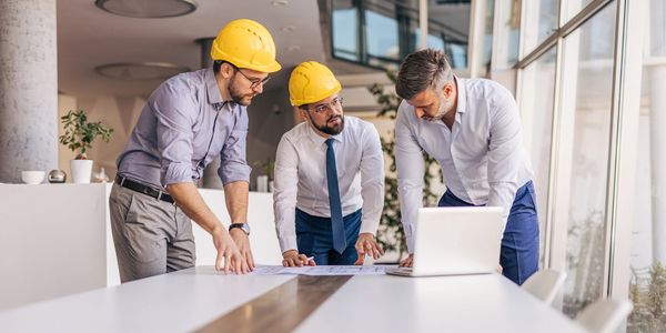 Three businessmen with yellow helmets discussing plans at office.