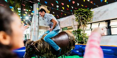 Man enjoying a mechanical bull ride at a festive outdoor event.