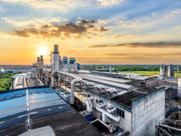 Industrial factory complex at sunset with lush green fields in the background.
