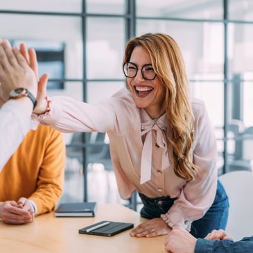 A woman happily high-fiving a colleague in a modern office.