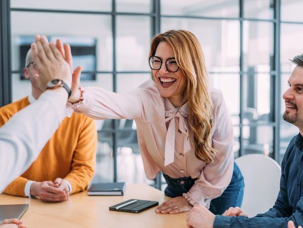 Colleagues celebrating a success with high fives in a modern office.