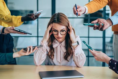 Mujer estresada rodeada de personas con dispositivos electrónicos.