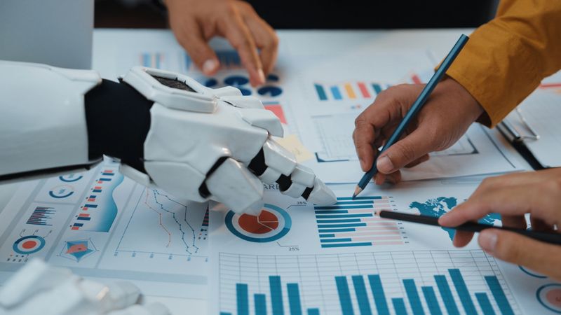 A human hand and a robotic hand work together on data analysis, surrounded by graphs and charts. This scene embodies the future of teamwork in a digital workspace.Noogenesis