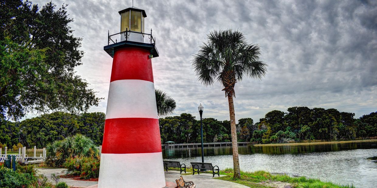 Red and white lighthouse near a lakeside with palm trees.