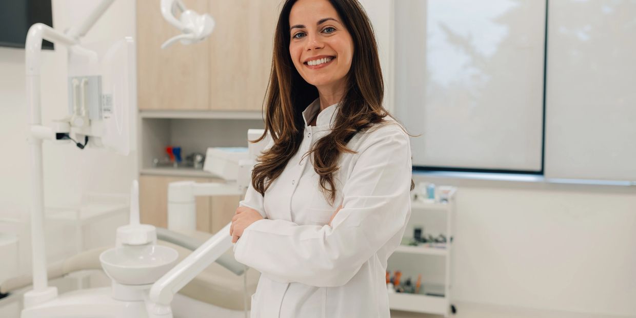 Smiling female dentist in white coat standing confidently in dental clinic.