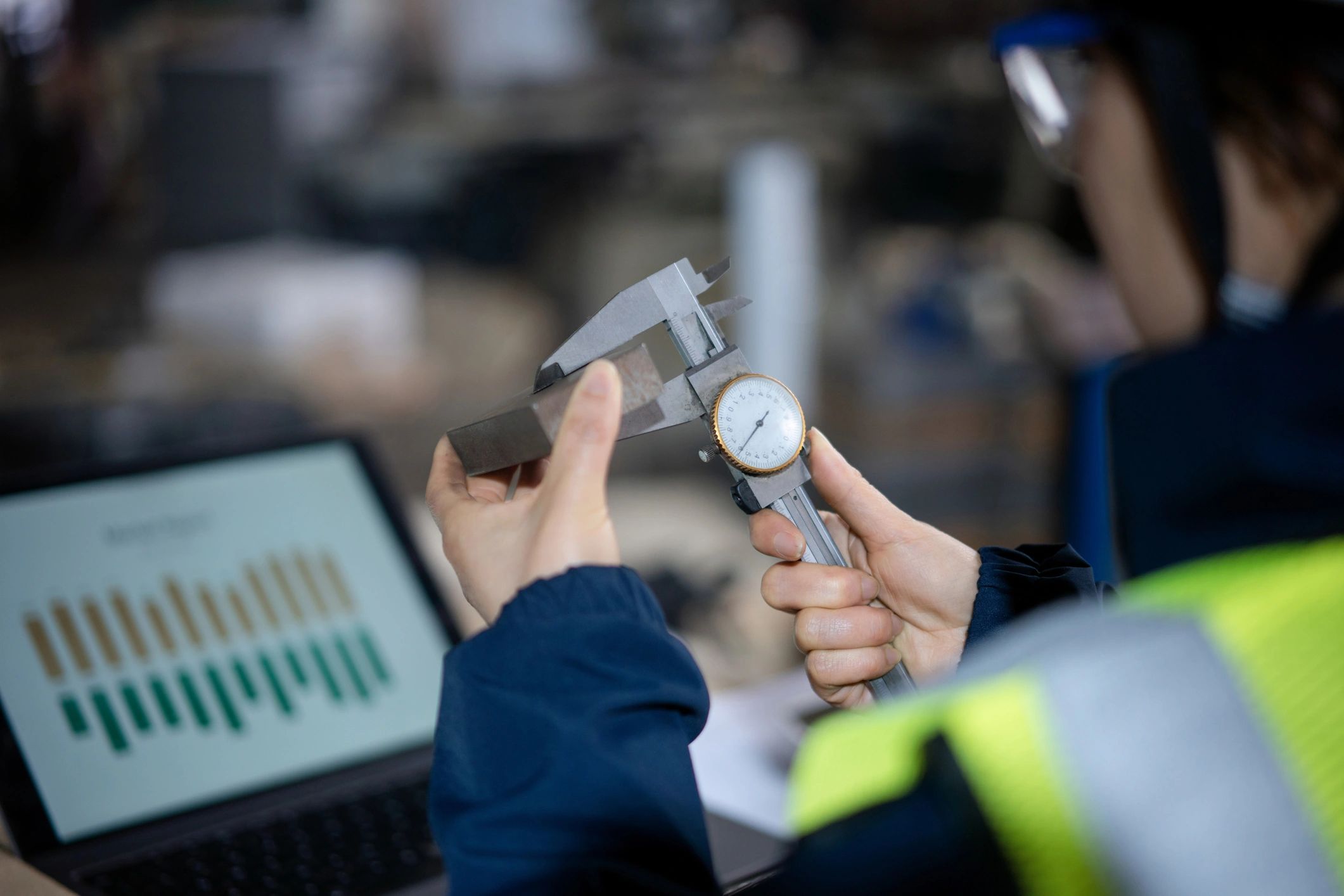 Person measuring a block with a caliper near a laptop.