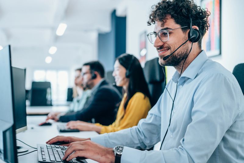 Shot of call center operators working in the office. Call center agent working with his colleagues in modern office. Smiling handsome businessman working in call center.