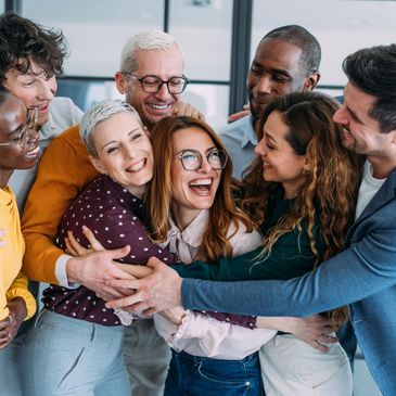 A diverse group of coworkers sharing a joyful group hug in an office setting.