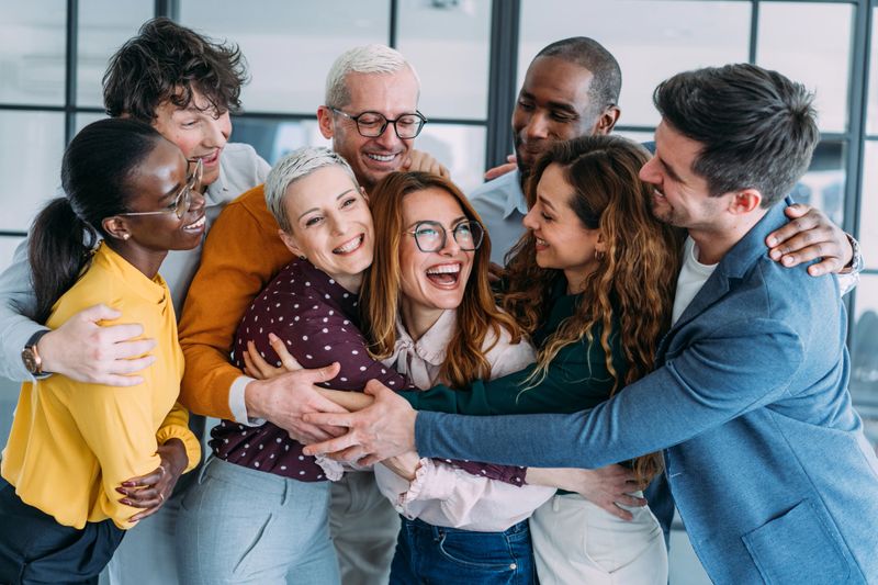 Shot of a business people embracing each other in modern office. Colleagues hugging and celebrating in the office.