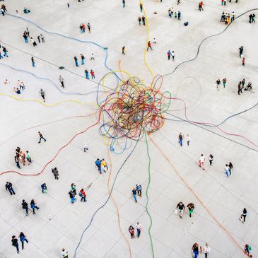 People walk around colorful cables spread out from a central knot on a large concrete surface.