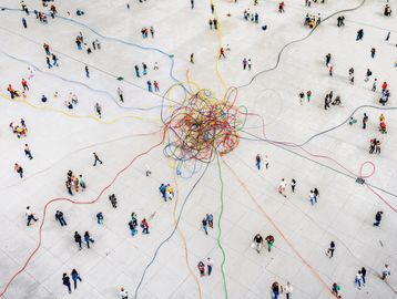 Aerial view of people connected by colorful tangled strings on a white surface.