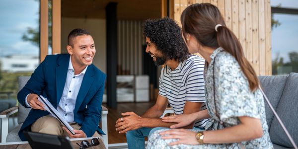 Three people engaged in a friendly outdoor conversation, with one holding a clipboard.