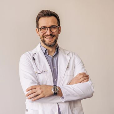 Smiling male doctor in a white coat with arms crossed.