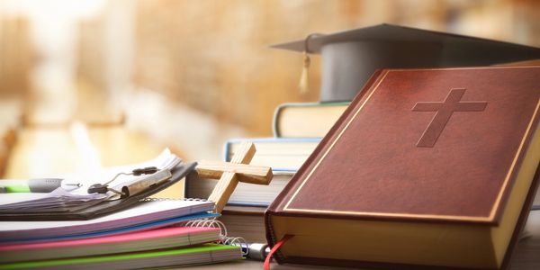 Bible, cross, and graduation cap on desk.