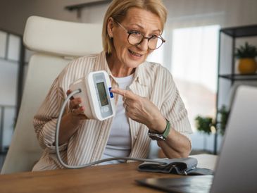 Senior woman using a digital blood pressure monitor at home.
