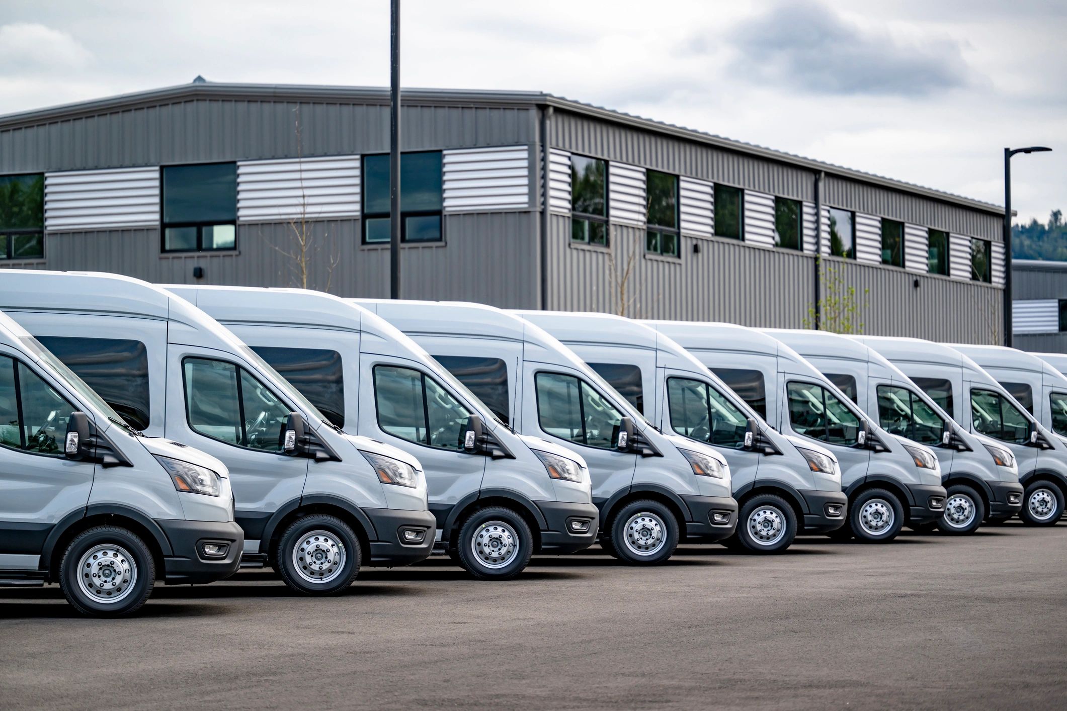 A row of white delivery vans parked outside a warehouse.