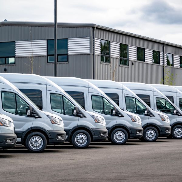 Line of white cargo vans parked outside a warehouse.