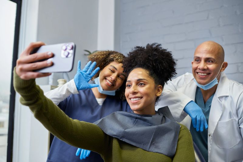 A dental patient poses for a selfie accompanied by two smiling dental professionals. The scene reflects a friendly and welcoming atmosphere at a modern clinic, emphasizing positivity and personalized care.