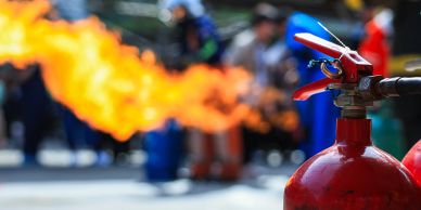Fire extinguisher with flames and people blurred in background.