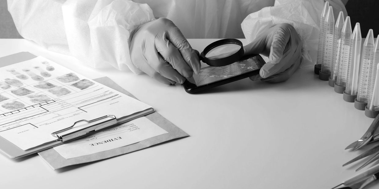 Forensic expert examines a cracked phone with a magnifying glass in a lab setting.