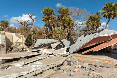 Collapsed house with debris under clear blue sky and palm trees.