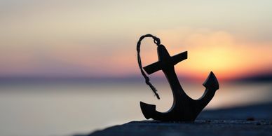 Silhouette of an anchor against a sunset background.