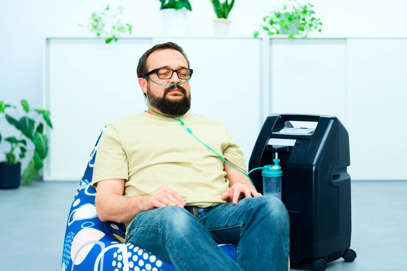 Oxygen therapy, supplemental oxygen. Man inhaling oxygen through nasal cannula attached to concentrator machine.
