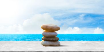 Stack of four smooth stones by the ocean under a blue sky.