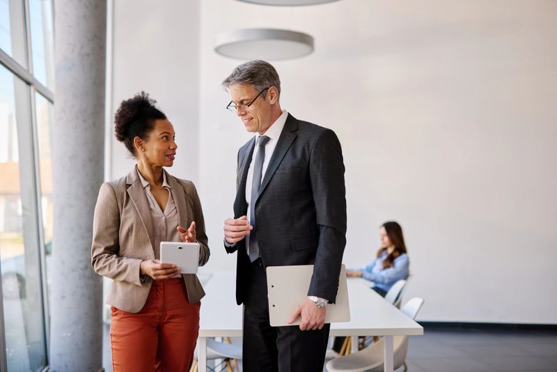 Two business people are discussing a project in a modern office, using a digital tablet and a clipboard, collaborating and sharing ideas in a professional environment