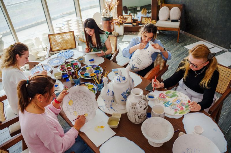 A group of people of different races and ages take part in a tile painting therapy class