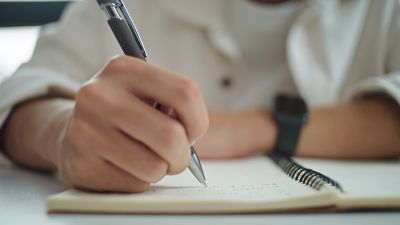 Person writing notes in a spiral notebook with a pen.