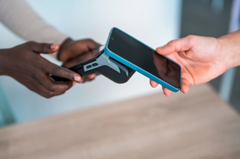 Close-up of two hands, one dark-skinned and one light-skinned, completing a cashless transaction using a smartphone and payment terminal in a minimalist boutique setting.