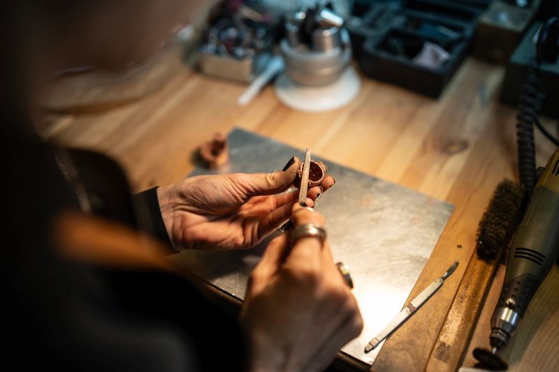 Close-up of a craftsman working meticulously on a piece of metal jewelry, showcasing skill and attention to detail in a workshop setting.