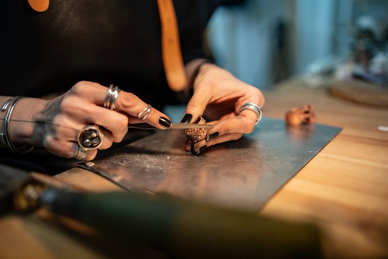 A skilled craftsperson's hands creating intricate jewelry pieces on a wooden workbench with tools.