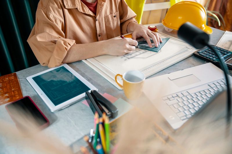 Young Man Architect drawing house plan using ruler, working in his office at construction site
