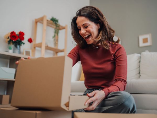Happy woman opening a cardboard box at home.
