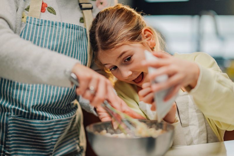 Grandmother and granddaughter whisking ingredients in a bowl, baking together in the kitchen