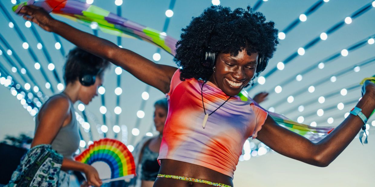 Joyful person dancing with headphones and colorful scarf under string lights.