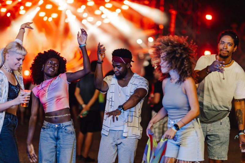 Group of young people dancing and having fun together at an outdoor music festival, enjoying the vibrant atmosphere and live performance under colorful stage lights