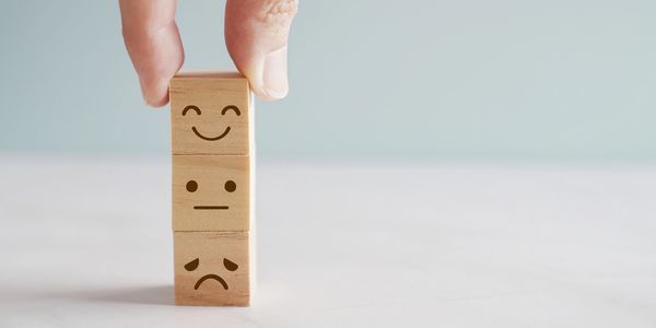 Fingers stacking three small wooden blocks with  line drawn faces each conveying different emotions