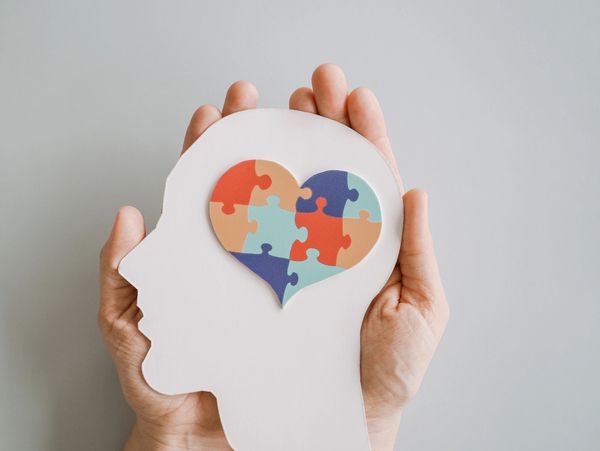 Hands holding a head silhouette and a heart puzzle.