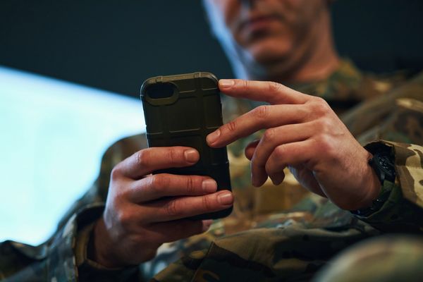 Soldier in uniform using a smartphone, supporting CFDay's defense and national security mission.