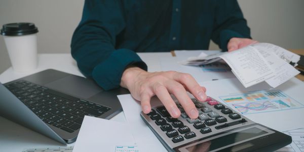 Person calculating expenses with a calculator and receipts at a desk.